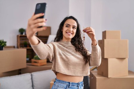 Téléchargez les photos : Jeune femme hispanique faire selfie par le smartphone tenant la clé à la nouvelle maison - en image libre de droit