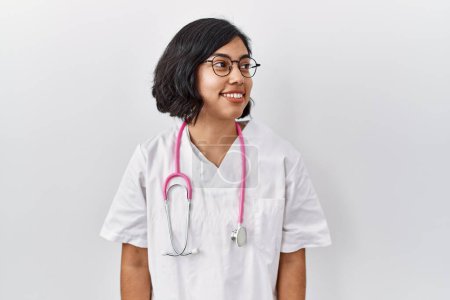 Téléchargez les photos : Jeune médecin hispanique femme portant stéthoscope sur fond isolé regardant de côté avec le sourire sur le visage, expression naturelle. riant confiant. - en image libre de droit