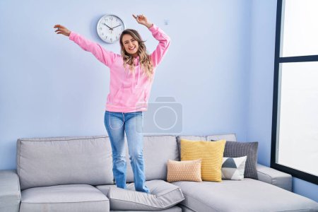Téléchargez les photos : Jeune femme écoutant de la musique et dansant sur le canapé à la maison - en image libre de droit