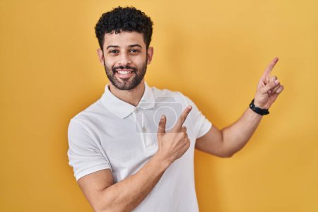 Photo for Arab man standing over yellow background smiling and looking at the camera pointing with two hands and fingers to the side. - Royalty Free Image