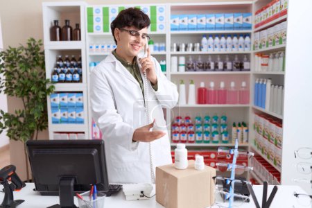 Téléchargez les photos : Pharmacien homme non binaire parlant sur téléphone tenant bouteille pilules à la pharmacie - en image libre de droit