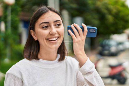 Téléchargez les photos : Jeune femme hispanique souriant confiant écoute message audio par le smartphone au parc - en image libre de droit