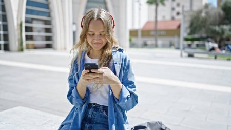 Téléchargez les photos : Jeune étudiante blonde utilisant un smartphone et un casque à l'université - en image libre de droit