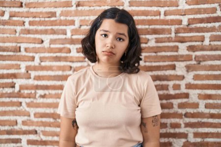 Téléchargez les photos : Jeune femme hispanique debout sur le mur de briques déprimé et inquiet pour la détresse, pleurer en colère et peur. triste expression. - en image libre de droit