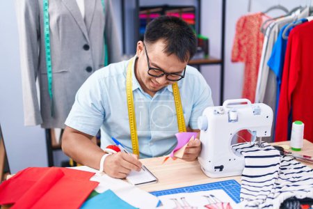 Photo for Young chinese man tailor writing on notebook holding cloth at tailor shop - Royalty Free Image