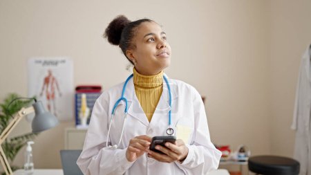 Foto de Mujer afroamericana joven médico usando smartphone en la clínica - Imagen libre de derechos