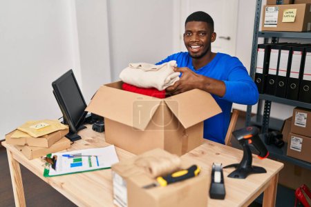 Téléchargez les photos : Jeune homme afro-américain commerce électronique travailleur d'affaires emballage vêtements paquet ordre au bureau - en image libre de droit