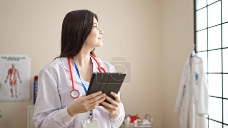 Photo for Young beautiful hispanic woman doctor smiling confident using touchpad at clinic - Royalty Free Image