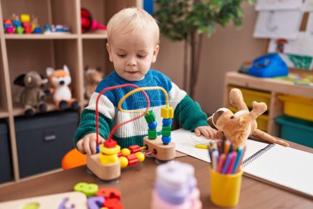 Foto de Adorable chico caucásico jugando con juguetes sentados en la mesa en el jardín de infantes - Imagen libre de derechos