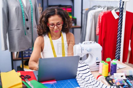 Téléchargez les photos : Middle age woman tailor smiling confident using laptop at clothing factory - en image libre de droit
