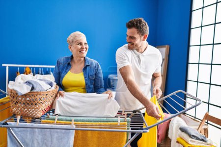 Foto de Madre e hijo sonriendo confiados colgando ropa en el tendedero en la sala de lavandería - Imagen libre de derechos