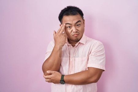 Photo for Chinese young man standing over pink background shooting and killing oneself pointing hand and fingers to head like gun, suicide gesture. - Royalty Free Image