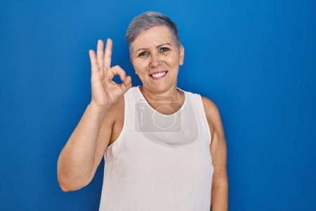 Photo for Middle age caucasian woman standing over blue background smiling positive doing ok sign with hand and fingers. successful expression. - Royalty Free Image