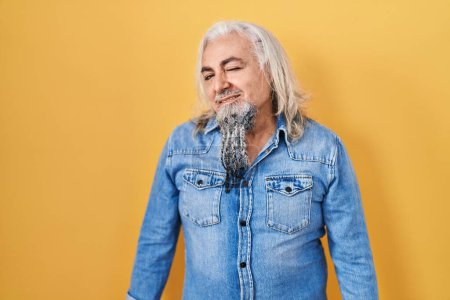 Photo for Middle age man with grey hair standing over yellow background winking looking at the camera with sexy expression, cheerful and happy face. - Royalty Free Image