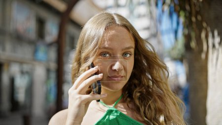 Téléchargez les photos : Jeune femme blonde parlant sur smartphone avec une expression sérieuse à la rue - en image libre de droit