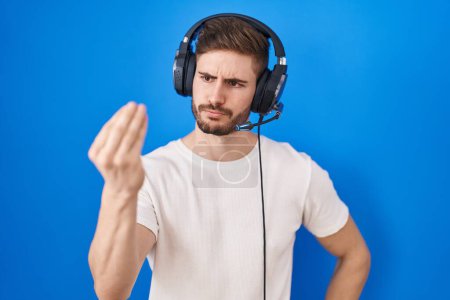 Téléchargez les photos : Homme hispanique avec barbe écoutant de la musique portant des écouteurs faire geste italien avec la main et les doigts expression confiante - en image libre de droit