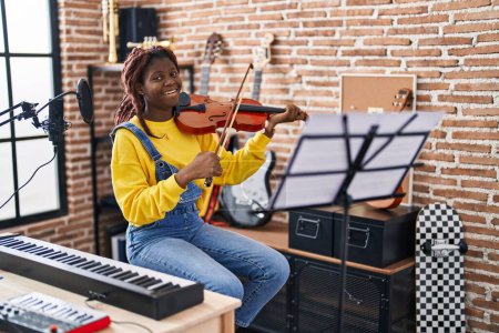 Foto de Músico afroamericano sonriendo confiado tocando violín en estudio de música - Imagen libre de derechos