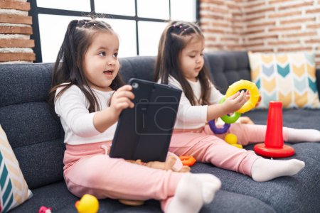 Photo for Adorable twin girls playing with hoops game using touchpad at home - Royalty Free Image