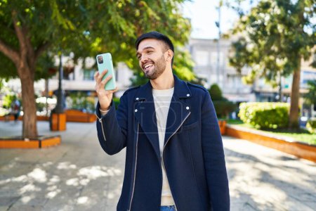 Foto de Joven hombre hispano sonriendo confiado usando smartphone en el parque - Imagen libre de derechos