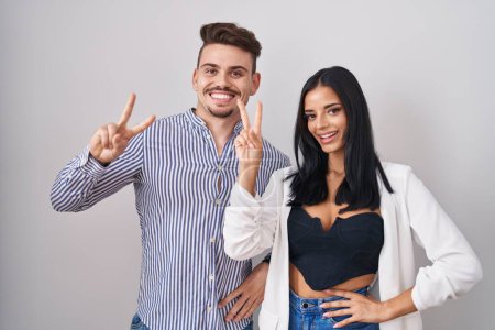 Téléchargez les photos : Young hispanic couple standing over white background smiling looking to the camera showing fingers doing victory sign. number two. - en image libre de droit