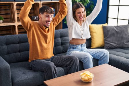 Téléchargez les photos : Jeune homme et femme couple jouer jeu vidéo assis sur canapé à la maison - en image libre de droit