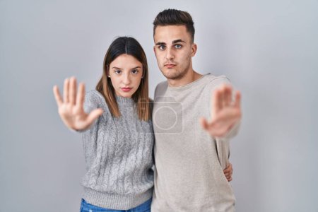 Photo for Young hispanic couple standing over white background doing stop sing with palm of the hand. warning expression with negative and serious gesture on the face. - Royalty Free Image
