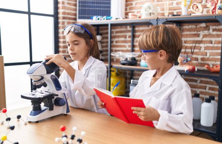 Téléchargez les photos : Adorables garçons étudiants utilisant des notes de microscope écriture à la salle de classe de laboratoire - en image libre de droit