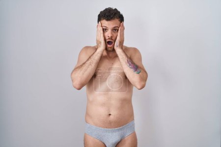Photo for Young hispanic man standing shirtless wearing underware afraid and shocked, surprise and amazed expression with hands on face - Royalty Free Image