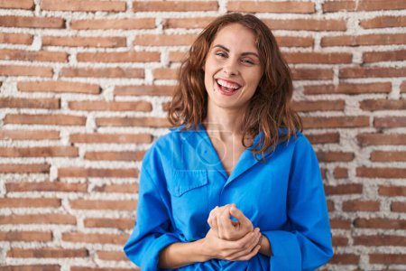 Téléchargez les photos : Belle femme brune debout sur un mur de briques avec les mains jointes et les doigts croisés souriant détendu et joyeux. succès et optimisme - en image libre de droit