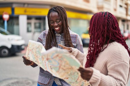 Foto de Mujeres afroamericanas amigas sonriendo confiadas mirando mapa de la ciudad en la calle - Imagen libre de derechos