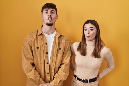 Photo for Young hispanic couple standing over yellow background making fish face with lips, crazy and comical gesture. funny expression. - Royalty Free Image