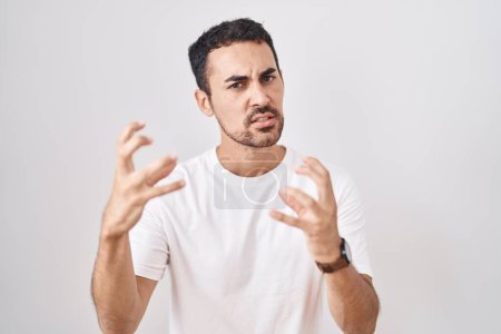 Photo for Handsome hispanic man standing over white background shouting frustrated with rage, hands trying to strangle, yelling mad - Royalty Free Image