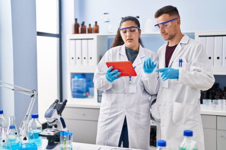 Téléchargez les photos : Man and woman wearing scientist uniform using touchpad at laboratory - en image libre de droit