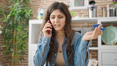 Foto de Joven hermosa mujer hispana hablando en un teléfono inteligente con tarjeta de crédito con expresión de enojo en el comedor - Imagen libre de derechos
