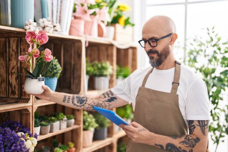 Photo for Young bald man florist using touchpad holding plant at florist - Royalty Free Image