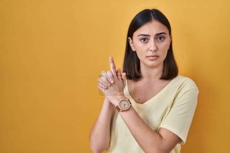 Photo for Hispanic girl wearing casual t shirt over yellow background holding symbolic gun with hand gesture, playing killing shooting weapons, angry face - Royalty Free Image