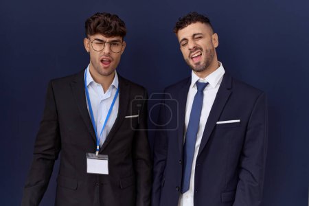 Téléchargez les photos : Deux hommes d'affaires hispaniques portant des vêtements d'affaires clin d'oeil en regardant l'appareil photo avec une expression sexy, gai et heureux visage. - en image libre de droit