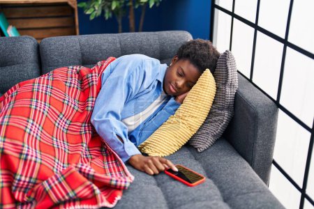 Foto de Mujer afroamericana tumbada en el sofá durmiendo apagar la alarma del teléfono inteligente en casa - Imagen libre de derechos