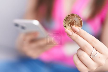 Joven mujer caucásica usando teléfono inteligente celebración uniswap moneda en casa