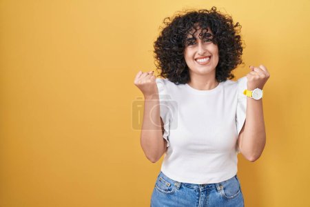 Téléchargez les photos : Jeune femme du Moyen-Orient debout sur fond jaune célébrant surpris et étonnés pour le succès avec les bras levés et les yeux ouverts. concept gagnant. - en image libre de droit