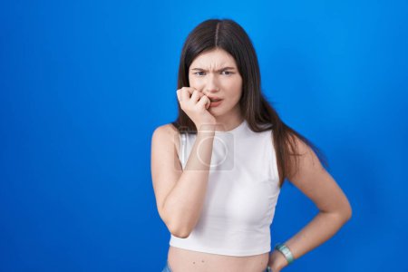 Photo for Young caucasian woman standing over blue background looking stressed and nervous with hands on mouth biting nails. anxiety problem. - Royalty Free Image
