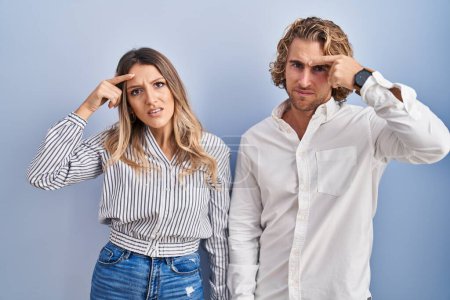 Photo for Young couple standing over blue background pointing unhappy to pimple on forehead, ugly infection of blackhead. acne and skin problem - Royalty Free Image