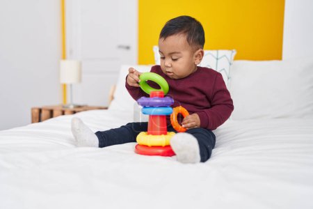 Téléchargez les photos : Adorable garçon hispanique jouant avec cerceaux jeu assis sur le lit dans la chambre - en image libre de droit