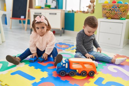 Foto de Adorable niño y niña jugando con coches juguete sentado en el suelo en el jardín de infantes - Imagen libre de derechos