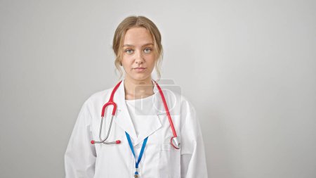 Foto de Joven doctora rubia de pie con expresión seria sobre fondo blanco aislado - Imagen libre de derechos