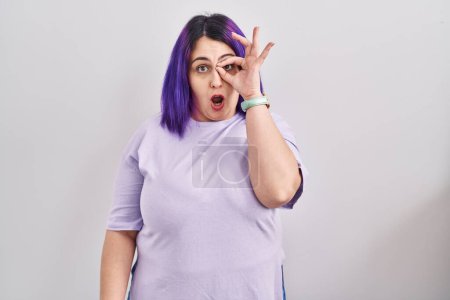 Photo for Plus size woman wit purple hair standing over isolated background doing ok gesture shocked with surprised face, eye looking through fingers. unbelieving expression. - Royalty Free Image