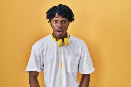 Téléchargez les photos : Jeune homme africain avec dreadlocks debout sur fond jaune peur et choqué avec surprise et expression étonnante, peur et visage excité. - en image libre de droit