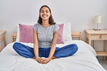 Foto de Mujer afroamericana joven haciendo ejercicio de yoga sentada en la cama en el dormitorio - Imagen libre de derechos
