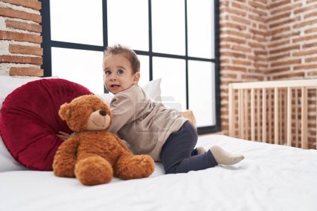Photo for Adorable hispanic boy sitting on bed with teddy bear at bedroom - Royalty Free Image