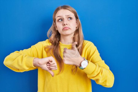 Photo for Young caucasian woman standing over blue background doing thumbs up and down, disagreement and agreement expression. crazy conflict - Royalty Free Image